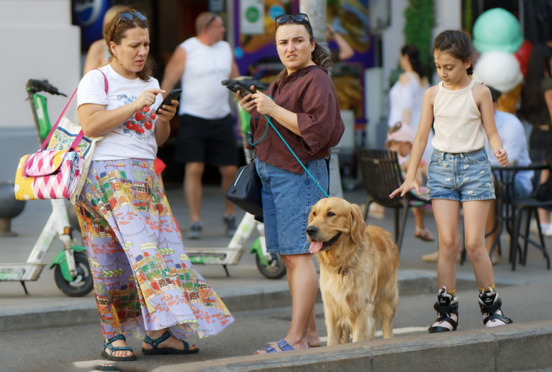 25 - Several people and a dog gathered on a pedestrian street, with a colorful patterned skirt visible in the foreground